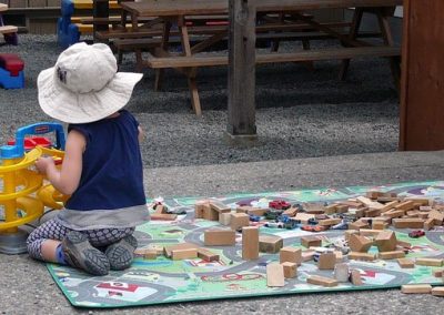 A child playing with wooden blocks on a play mat outdoors