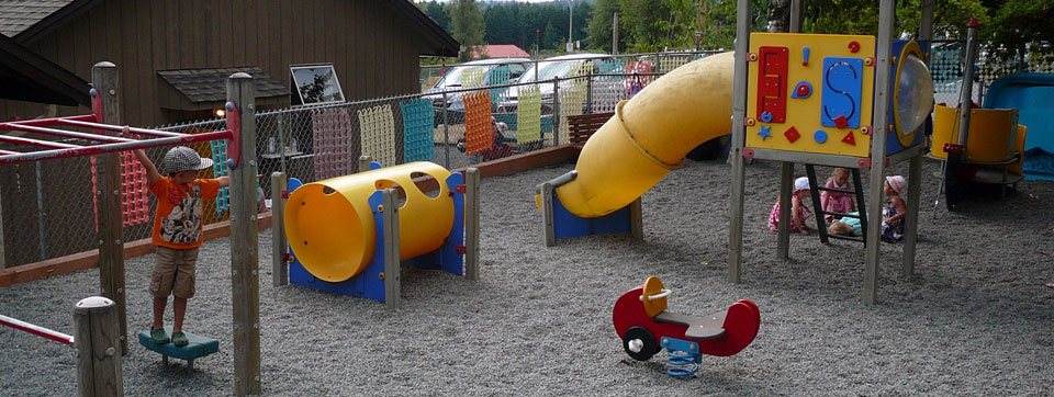 Children playing in the fenced outdoor play yard with a yellow slide